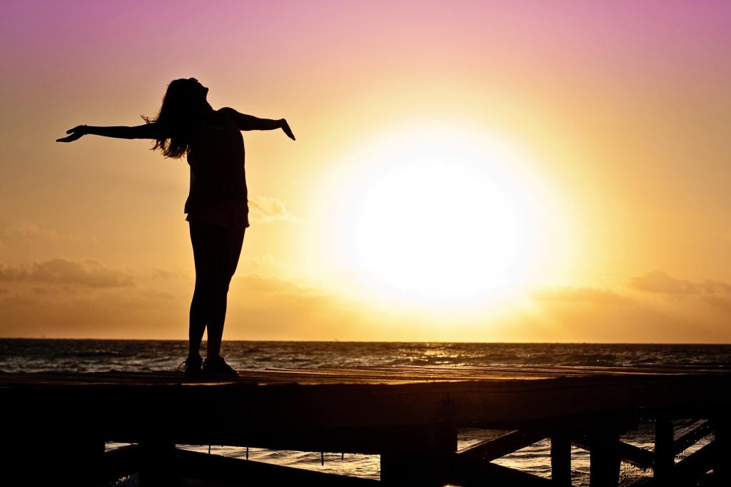 woman standing on bridge holding arms out at sunset